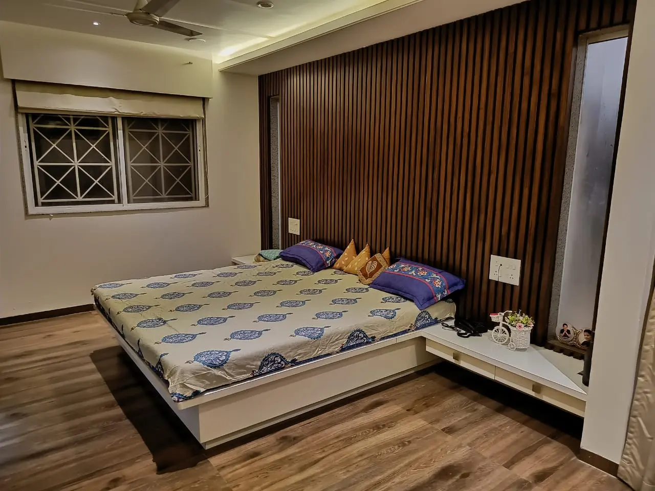 a bed with pillows and a wooden louvers on headboard showing best interior desgn pune